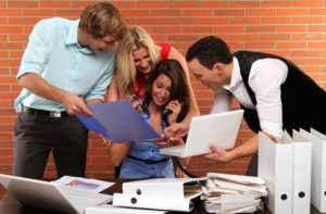 A female teacher is sitting in front of an office table while three adult students is showing her their project. A female teacher is sitting in front of an office table while three adult students is showing her their project.