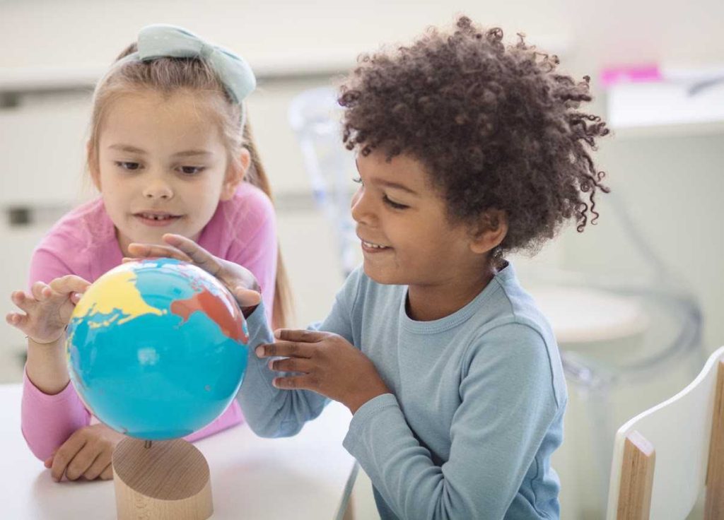 Two kids pointing at a world map globe on the table