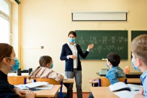 Female teacher in front of the classroom teaching young students while wearing face masks
